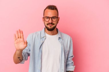 Pembe arka planda izole edilmiş beyaz dövmeli genç bir adam gülümseyerek beş numarayı parmaklarıyla gösteriyor..