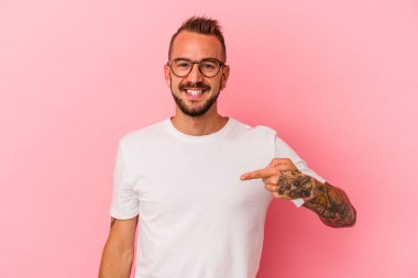 Pembe arkaplanda dövmeleri olan beyaz bir adam gömleğinin fotokopi odasını işaret ediyor, gururlu ve kendinden emin.