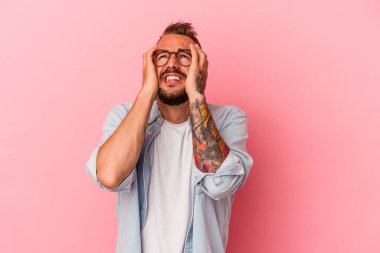 Pembe arka planda, ağlayan ve sızlanan, dövmeleri olan beyaz bir genç adam..