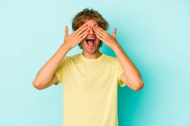 Mavi arka planda soyutlanmış beyaz makyajlı genç bir adam elleriyle gözlerini kapatıyor, gülümseyerek bir sürpriz bekliyor..