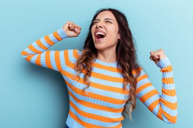 Mavi arka planda izole edilmiş genç Meksikalı kadın zaferden sonra yumruğunu kaldırıyor, kazanan konsept.