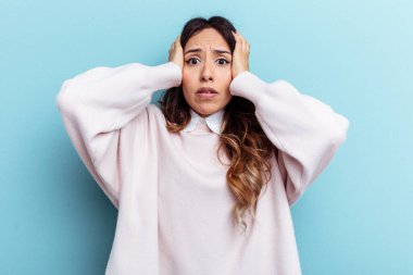 Genç Meksikalı bir kadın mavi arka planda izole edilmiş kulakları kulaklarıyla kapatıyor ve çok fazla ses duymamaya çalışıyor..