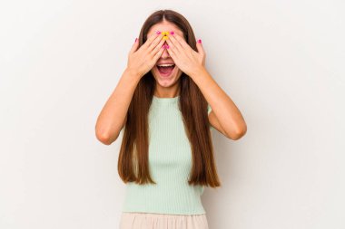 Beyaz arka planda soyutlanmış beyaz tenli genç bir kadın elleriyle gözlerini kapatıyor, geniş bir gülümsemeyle bir sürpriz bekliyor..