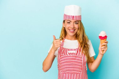 Kafkas dondurma üreticisi kadın elinde dondurma tutarken mavi arka planda izole edilmiş gülümsüyor ve başparmağını kaldırıyor.