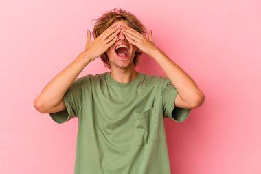 Pembe arka planda soyutlanmış beyaz makyajlı genç bir adam elleriyle gözlerini kapatıyor, gülümseyerek bir sürpriz bekliyor..