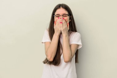 Sarı arka planda izole edilmiş genç beyaz kadın bir şeye gülüyor, elleriyle ağzını kapatıyor..