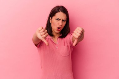 Pembe arka planda izole edilmiş genç beyaz kadın baş parmağını aşağı gösteriyor ve hoşlanmadığını ifade ediyor..