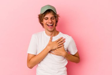 Pembe arka planda soyutlanmış beyaz makyajlı genç bir adam gülüyor, ellerini yüreğine koyuyor, mutluluk kavramını koruyor..