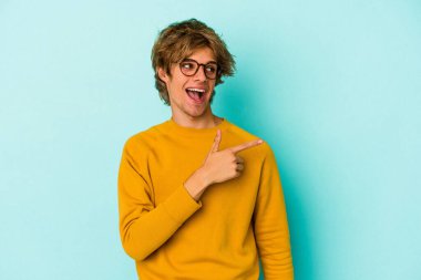 Mavi arka planda soyutlanmış beyaz makyajlı genç bir adam gülümsüyor, neşeli ve keyifli görünüyor..