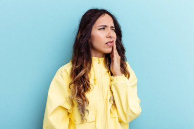 Mavi arka planda izole edilmiş genç Meksikalı kadın güçlü bir diş ağrısı ve azı dişi ağrısı var..