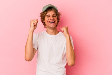 Pembe arka planda soyutlanmış beyaz tenli genç bir adam zaferi, tutkuyu ve coşkuyu kutluyor, mutlu bir ifade..