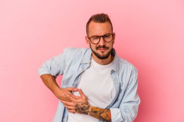 Pembe arka planda karaciğer ağrısı ve karın ağrısı olan beyaz dövmeli genç bir adam..