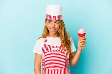 Kafkasyalı dondurma üreticisi kadın elinde dondurma tutuyor mavi arka planda, kafası karışmış, kararsız ve kendinden emin değil..