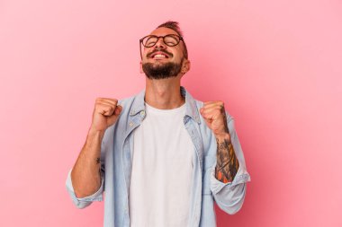 Pembe arka planda izole edilmiş dövmeleri olan beyaz bir adam zaferi, tutkuyu ve coşkuyu kutluyor..