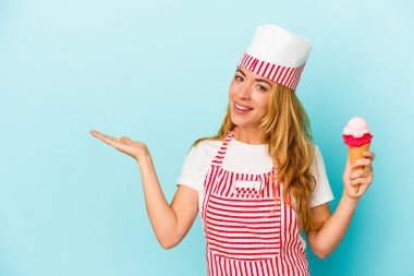 Kafkasyalı dondurma üreticisi kadın elinde dondurmayla mavi arka planda izole edilmiş bir şekilde avucunun içinde bir fotokopi alanı ve belinde bir el daha gösteriyor..