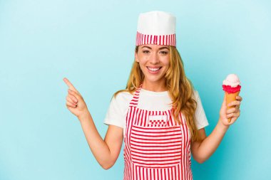 Kafkasyalı dondurma üreticisi kadın elinde dondurmayla mavi arka planda izole edilmiş gülümsüyor ve boş alanda bir şey gösteriyor..