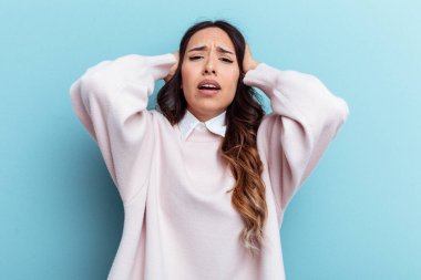 Mavi arka planda izole edilmiş genç Meksikalı kadın öfkeyle bağırıyor..