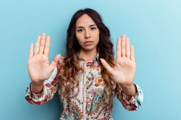 Mavi arka planda izole edilmiş genç Meksikalı kadın elini uzatmış, dur işareti göstererek seni engelliyor..
