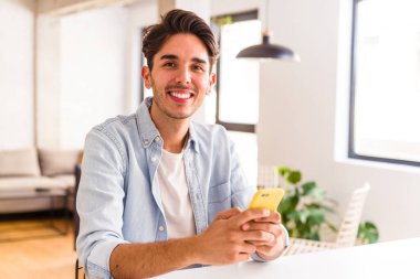 Genç melez adam mutfakta telefonla konuşuyor.