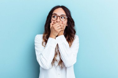 Genç Meksikalı bir kadın mavi arka planda izole edilmiş. Düşünceli bir şekilde bir fotokopi odasına bakıyor. Ağzını eliyle kapatıyor..