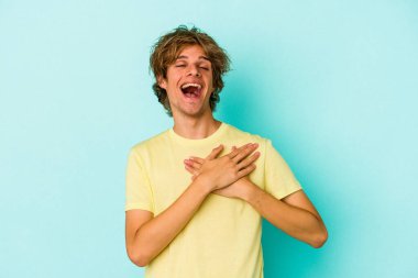 Mavi arka planda mahsur kalmış beyaz tenli genç bir adam dost bir ifadeye sahip, avuçlarını göğsüne bastırıyor. Aşk konsepti.