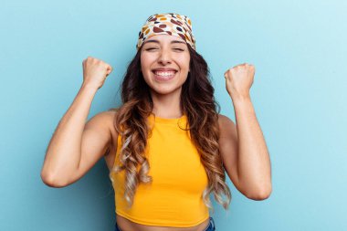 Mavi arka planda izole edilmiş genç Meksikalı kadın tasasız ve heyecanlı bir şekilde tezahürat yapıyor. Zafer konsepti.