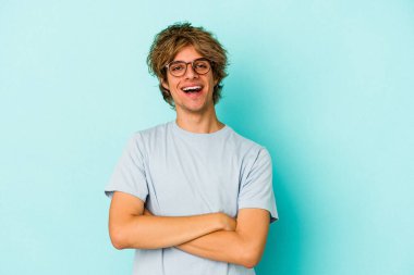 Mavi arka planda soyutlanmış, kendine güveni tam, kararlılıkla kollarını kavuşturan beyaz bir genç..