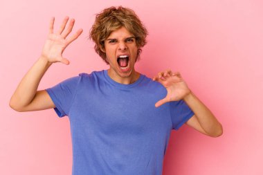 Pembe arka planda soyutlanmış beyaz makyajlı genç bir adam pençelerini kedi taklidi yaparken gösteriyor, agresif bir hareket..