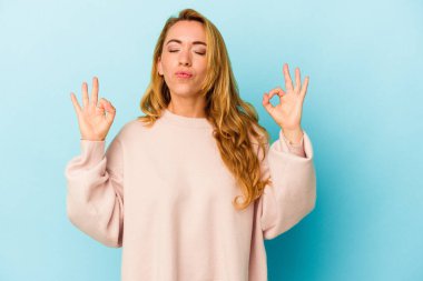 Beyaz kadın, mavi arka planda izole edilmiş yoğun çalışma gününden sonra rahatlıyor, yoga yapıyor..