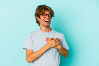 Mavi arka planda soyutlanmış beyaz makyajlı genç bir adam gülüyor, ellerini yüreğine koyuyor, mutluluk kavramını koruyor..