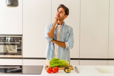 Genç melez adam öğle yemeği için salata hazırlıyor. Şüpheli ve şüpheci bir ifadeyle yana bakıyor..