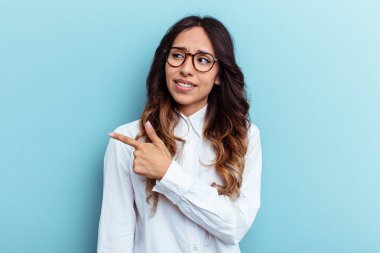 Mavi arka planda izole edilmiş genç Meksikalı kadın gülümsüyor ve boş alanda bir şeyler gösteriyor..