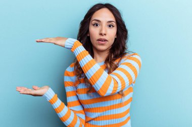 Mavi arka planda izole edilmiş genç Meksikalı kadın elleri arasında bir kopya alanı tutarken şok ve hayrete düştü..