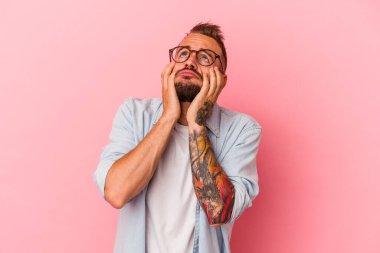 Pembe arka planda izole edilmiş dövmeleri olan genç, beyaz bir adam ağlıyor, bir şeyden mutsuz, acı ve kafa karışıklığı konsepti var..