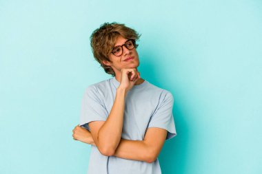 Makyajlı genç beyaz adam mavi arka planda izole edilmiş düşünüyor ve yukarı bakıyor, yansıtıyor, düşünüyor, hayal kuruyor..