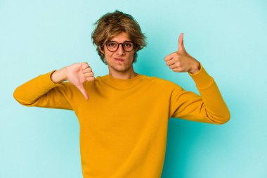 Mavi arka planda soyutlanmış beyaz makyajlı genç bir adam baş parmağını kaldırıyor ve baş parmağını eğiyor, zor seçim kavramı.