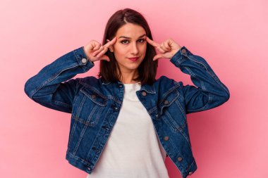 Pembe arka planda izole edilmiş genç beyaz kadın bir göreve odaklanmış, parmaklarını işaret ediyor..