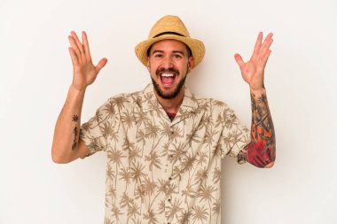 Beyaz arka planda izole edilmiş yazlık giysiler giyen beyaz dövmeli genç beyaz adam hoş bir sürprizle karşılaşıyor, heyecanlı ve el kaldırıyor..