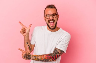 Pembe arka planda izole edilmiş beyaz dövmeli genç bir adam işaret parmaklarıyla fotokopi alanını işaret ederek heyecan ve arzusunu ifade ediyor..