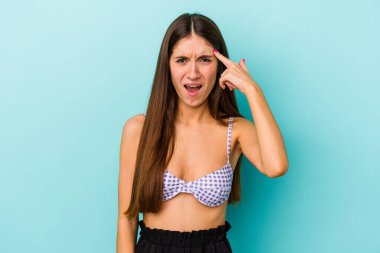 Mavi arka planda izole edilmiş bikini giyen beyaz bir kadın işaret parmağıyla yaptığı hayal kırıklığını gösteriyor..