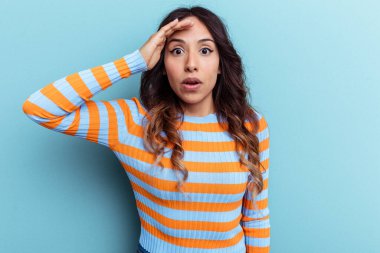 Mavi arka planda izole edilmiş genç Meksikalı kadın yüksek sesle bağırıyor, gözlerini açık ve ellerini gergin tutuyor..