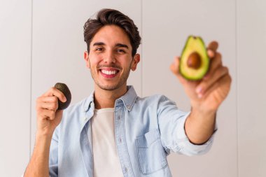 Genç melez adam mutfağında avokado tutuyor.