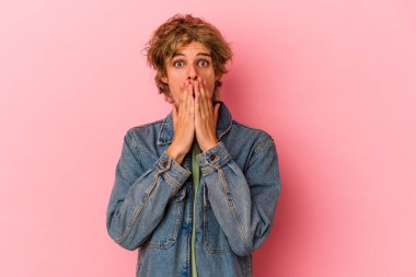 Pembe arka planda soyutlanmış beyaz tenli genç bir adam elleriyle ağzını kapatarak şoka girdi..