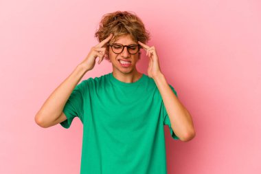 Makyajlı beyaz bir adam pembe arka planda izole edilmiş tapınaklara dokunuyor ve baş ağrısı çekiyor..