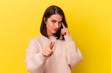 Sarı arka planda izole edilmiş genç beyaz bir kadın şakağı parmağıyla işaret ediyor, düşünüyor ve bir göreve odaklanıyor..