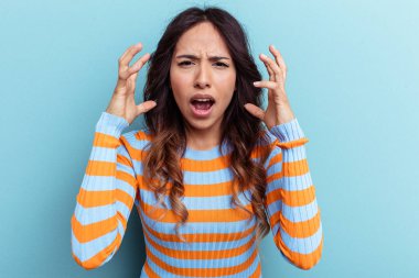 Mavi arka planda izole edilmiş genç Meksikalı kadın gergin elleriyle çığlık atıyor..