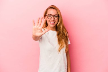 Kafkasyalı sarışın kadın pembe arka planda izole edilmiş gülümsüyor beş numarayı parmaklarıyla gösteriyor..