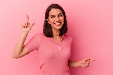 Pembe arka planda izole edilmiş genç beyaz kadın farklı kopya alanlarını gösteriyor, birini seçiyor, parmağıyla gösteriyor..