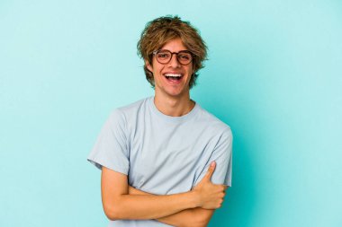 Makyajlı genç beyaz adam mavi arka planda izole edilmiş gülüyor ve eğleniyor..