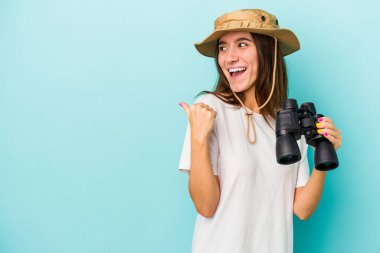 Dürbün tutan Kafkasyalı genç kaşif kadın mavi arka planda parmak uzakta, gülen ve kaygısız..